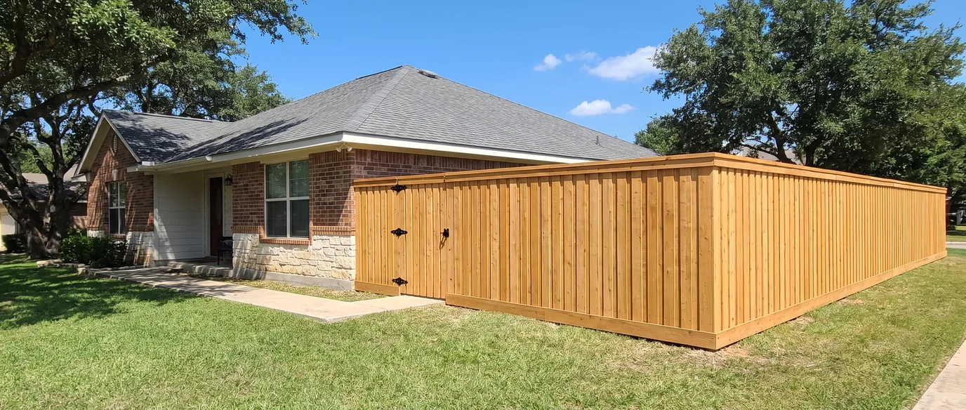 A new cedar privacy fence with a walk gate running from the corner of a brick and limestone ranch house across its side yard